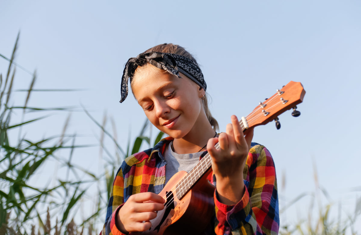 Young traveler playing a ukulele in tall grass while dreaming of teaching English in Japan without a degree