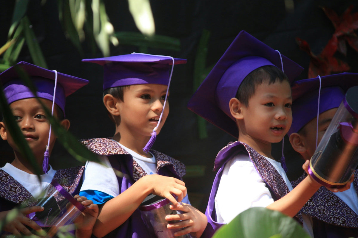 Young children in purple caps and gowns at a kindergarten graduation in Asia, where TEFL teachers are in demand