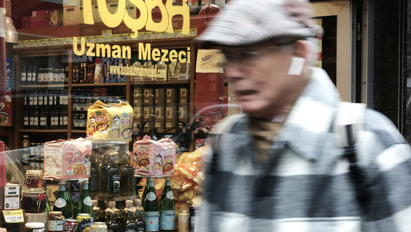 A man walking past a Turkish store window, where everyday grocery prices show the effect of inflation