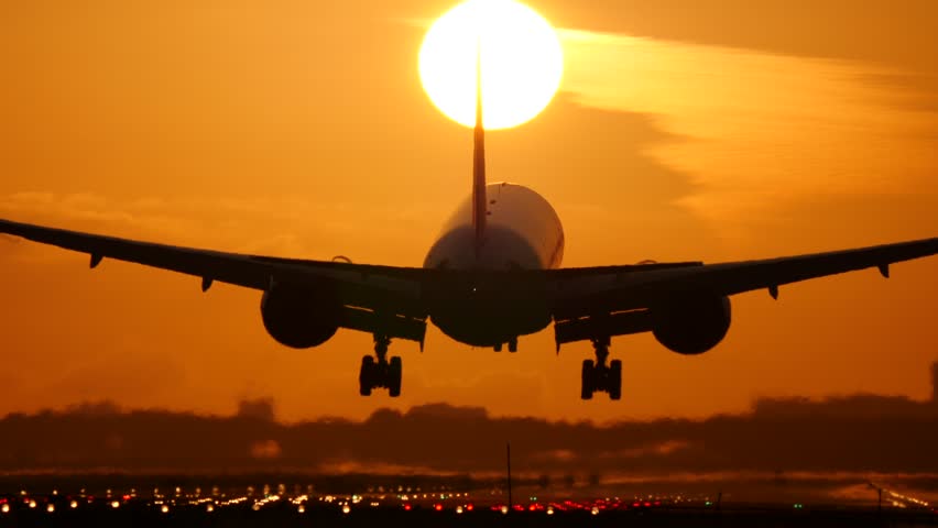 A plane landing while the sun is setting in the background